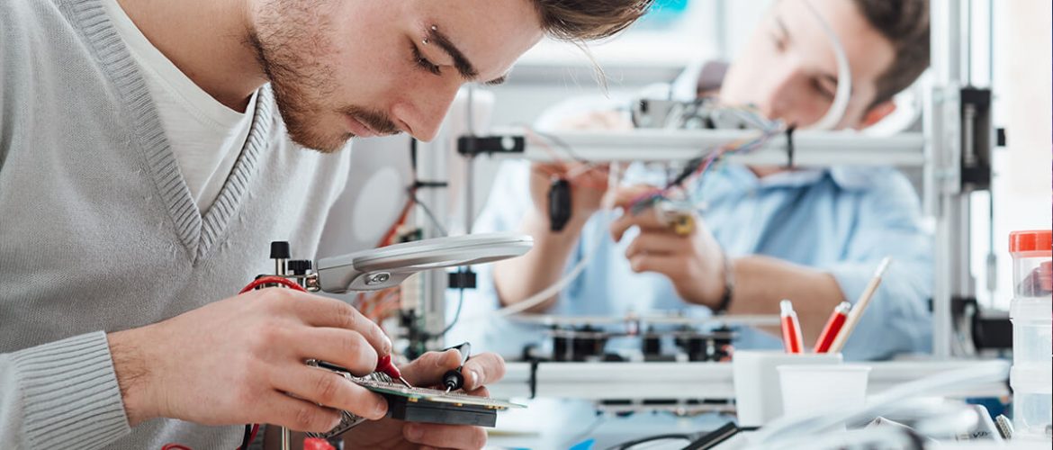 Two male engineers working in a lab with voltage and current tester and a 3D printer
