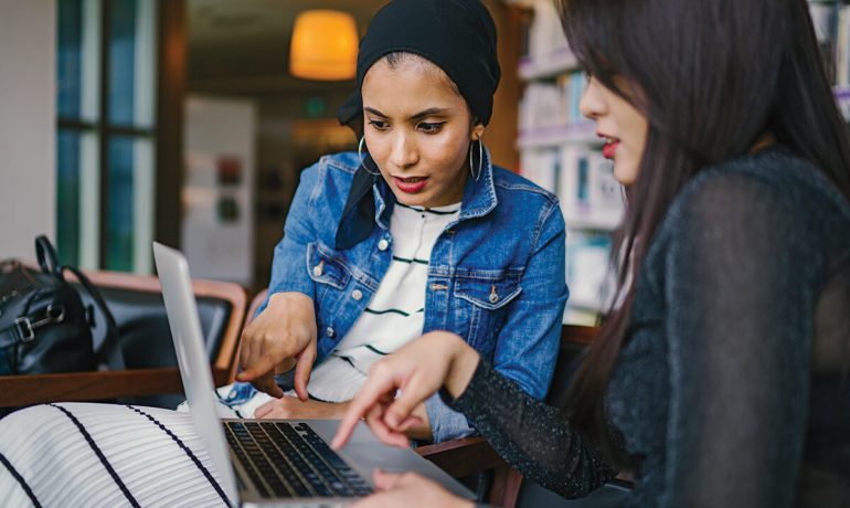 Two women working together on a laptop in the library