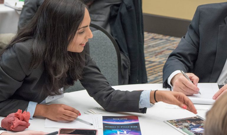 Woman discussing with small group at table during 2018 NASA iTech forum event